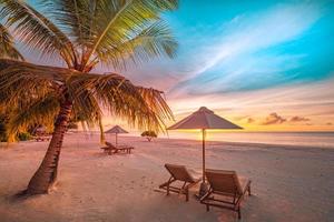 Wunderschöner tropischer Sonnenuntergangsstrand, ein paar Sonnenliegen, Sonnenschirme unter Palmen. weißer Sand, Meerblick mit Horizont, bunter Dämmerungshimmel, Ruhe und Entspannung. inspirierendes Strandresort-Hotel foto