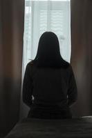 Silhouette einer jungen Frau im Schlafanzug vor dem Hintergrund eines Fensters zu Hause auf einem Bett mit saisonaler affektiver Störung oder Depression.. das Konzept der Winterdepression aufgrund von Sonnenlichtmangel foto