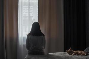 Silhouette einer jungen Frau im Schlafanzug vor dem Hintergrund eines Fensters zu Hause auf einem Bett mit saisonaler affektiver Störung oder Depression.. das Konzept der Winterdepression aufgrund von Sonnenlichtmangel foto