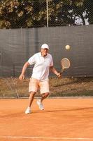 Älterer Tennisspieler in Sportkleidung in Aktion auf einem Sandtennisplatz foto