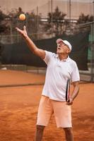 Älterer Tennisspieler in Sportkleidung in Aktion auf einem Sandtennisplatz foto