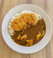 Japanischer Hähnchen-Katsu-Curry-Reis, frittiertes Hähnchenbrustfilet mit Rindfleisch, Karotten und Kartoffelcurry in schwarzer Platte auf Holztisch foto