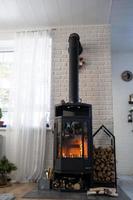 Schwarzer Ofen, Kamin im Inneren des Hauses im Loft-Stil. alternative umweltfreundliche heizung, warmes gemütliches zimmer zu hause, verbrennung von holz foto