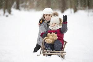 Zwei Brüder fahren auf einem alten Holzschlitten vor der Kulisse eines Winterwaldes. foto