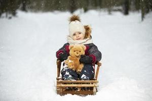 Ein kleiner Junge in warmer Kleidung sitzt in einem Holzschlitten vor dem Hintergrund der Winternatur. foto