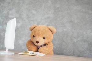 Teddybär, um Menschen zu imitieren. Setzen Sie sich mit einem Laptop und einem Notebook auf den Tisch. lernen im kindheitskonzept foto