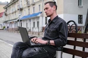 Ein junger Freiberufler arbeitet an einem Laptop in der Stadt. Online-Geschäft, Freiberufler, Fernarbeit. Aus-und Weiterbildung foto