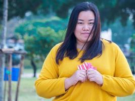 porträt mädchen asiatische frau eine menschen lange schwarze haare tragen ein gelbes langärmliges t-shirt. sitzen auf park garten stuhl lächeln hand hält recyceltes papier glücklich gefaltet in geschenkherz abendzeit foto