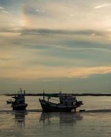 vertikale Bildansicht Atmosphäre Meer nimmt mit der Zeit ab Tag. Abends bei Sonnenuntergang können Sie zwei festgemachte Fischerboote und einen langen Sandstrand am Strand sehen, der in der Dämmerung schreit, der Himmel sieht wunderschön aus foto