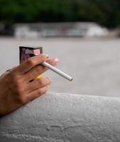 Nahaufnahme Hand Frau jugendlich junges Asien eine Person, die ein schwarzes Hemd trägt, halten das Rauchen der Zigarette weiße Farbe, die im Freien an der Wand steht foto