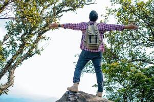 junger trekkingmann, der auf felsigem berggipfel steht foto