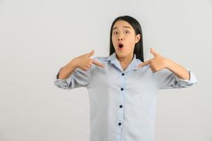 Porträt einer aufgeregten jungen asiatischen Frau im blauen Hemd, die mit dem Finger auf etwas zeigt, das auf weißem Hintergrund isoliert ist foto