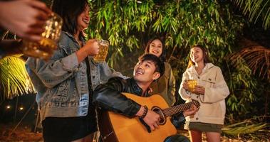 porträt einer glücklichen asiatischen gruppe von freunden, die spaß bei musik haben, die zusammen im freien essen und trinken - glückliche freundesgruppe, die bier röstet - menschen, essen, trinken, lebensstil, neujahrsfeierkonzept. foto
