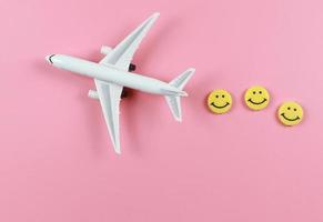 flache Lage des Flugzeugmodells mit drei lächelnden Gesichtern des gelben Kreises auf rosa Hintergrund. glückliches oder lustiges reisekonzept. foto