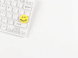 flache Lage des gelben Kreises lächelndes Gesicht auf weißer Computertastatur auf weißem Hintergrund. foto