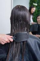 Friseur wendet eine Haarmaske auf glattes schwarzes Haar an. Haarpflege im Schönheitssalon. foto