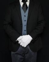 Butler in dunklem Anzug und weißen Handschuhen, die würdevoll die Aufmerksamkeit auf sich ziehen. konzept der dienstleistungsbranche und der professionellen gastfreundschaft. foto