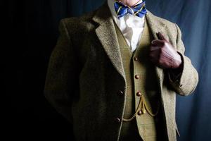 Porträt eines Mannes in Tweed-Anzug und Lederhandschuhen, die stolz auf schwarzem Hintergrund stehen. klassischer und exzentrischer englischer Gentleman. Retro-Stil und Vintage-Mode. foto