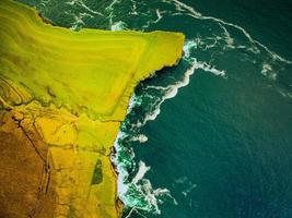 Luftaufnahme von oben wilde Küste Irlands mit Meereswellen stürzen entlang der Küste mit grün bewirtschafteten landwirtschaftlichen Flächen am Rand. Wild Atlantic Way Reiseroute entlang der Küste. foto