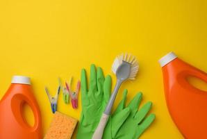 Gummigrüne Handschuhe zum Reinigen, orangefarbene Plastikflasche mit Reinigungsmittel, Bürste auf gelbem Hintergrund, Set foto