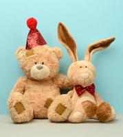 Teddybär mit Mütze und ein süßer Teddyhase mit langen Ohren, um den Hals ist ein roter Schmetterling gebunden foto
