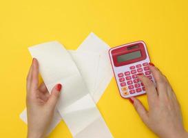 Zwei weibliche Hände halten Papierschecks und einen rosa Taschenrechner auf gelbem Hintergrund. das konzept der berechnung des budgets foto