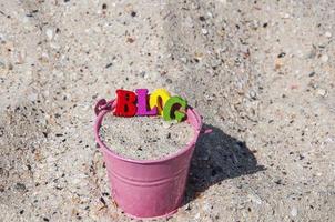 Word-Blog aus Holzbuchstaben in einem rosa Eimer mit Sand foto