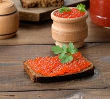 roter Lachskaviar liegt auf einem Stück Roggenbrot. brauner Holztisch foto