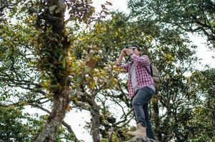 junger Rucksacktourist benutzt Kamera, um Bilder im Wald zu machen. foto