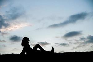 Schattenbild der entspannenden jungen Frau, die während des Sonnenuntergangs sitzt foto