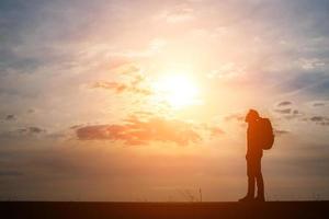 Schattenbild eines jungen Rucksacktouristenmannes, der während des Sonnenuntergangs geht foto