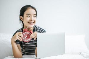 junge Frau sitzt auf ihrem Bett und hält einen Wecker foto