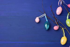 dekorative ostereier hängen an einem ast, blauer holzhintergrund foto