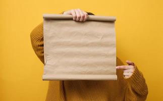 Frau im Orange Sweatshirt hält leer braun braun Kraft Papier rollen. Platz zum ein Inschrift, Werbung, Information foto