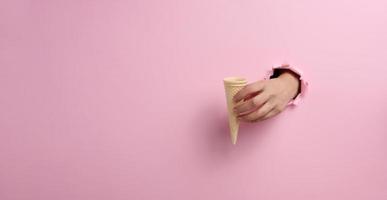 leeren Waffel Kegel Eis Sahne Tasse im ein Frau Hand kleben aus von ein zerrissen Loch im ein Rosa Papier foto