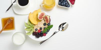 Tasse von schwarz Kaffee, ein Teller von Haferflocken und Frucht, Honig und ein Glas von Milch auf ein Weiß Tisch, ein gesund Morgen Frühstück, oben Aussicht foto