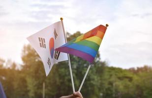 regenbogenflagge und südkoreanische nationalflagge in der hand halten, weicher und selektiver fokus, konzept zur feier von lgbtq plus im stolzmonat auf der ganzen welt. foto