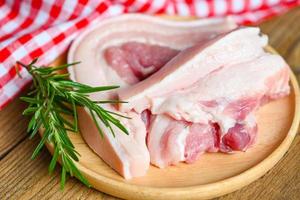 Schweinefleisch auf Holzplatte mit Rosmarin, frisches, rohes, durchwachsenes Schweinefleisch zum Kochen von Speisen, Schweinehaut Schweinehaut - Draufsicht foto