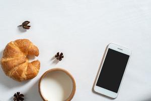 Draufsicht auf Tasse Milch, Notizbuch, Croissant auf Holztisch foto