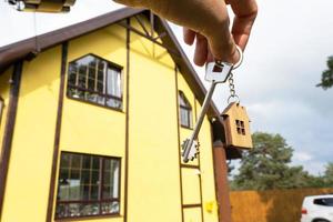 eine Hand mit den Schlüsseln zu einem neuen Haus auf dem Hintergrund eines unvollendeten Häuschens. Bauen, Projekt, Umzug in ein neues Zuhause, Hypothek, Miete und Kauf von Immobilien. zum Öffnen der Tür. Platz kopieren foto