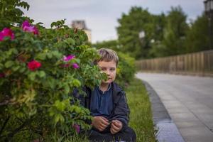 Porträt von ein Kind, ein Junge gegen das Hintergrund von Pflanzen im ein Open-Air Park. Kinder, Reise. Lebensstil im das Stadt. Center, Straßen. foto