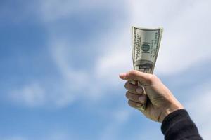 Hand mit Geld auf blauem Himmel Wolkenhintergrund foto