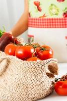 Korb von Tomaten mit ein Frau mit ein Schürze im das Hintergrund. Vertikale Bild. foto