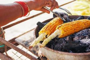 Maiskolben auf dem Grill. Nahaufnahme mit Hühneraugen und Händen. asiatisches, indisches und chinesisches Street Food. Trolley am Strand von Goa foto