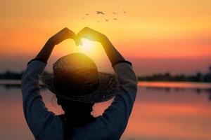 Liebe und glückliches Konzept, Silhouette der Frauen machen Herzform im Sonnenuntergang