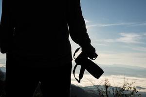 Schattenbild des jungen Fotografen, der eine Kamera mit Berglandschaft hält