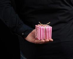 männlich Hand hält ein papierverpackt Box mit ein Geschenk hinter seine zurück foto