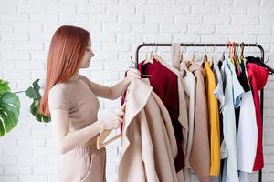 jung schön Frau tragen Beige Pastell- Mantel, Stehen in der Nähe von Kleider Gestell. Kleiderschrank Veränderung foto