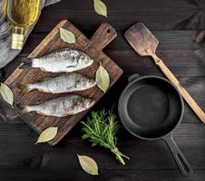 drei Fluss Fisch auf ein braun hölzern Tafel und ein schwarz Gusseisen braten schwenken foto