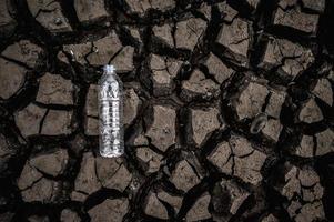 Wasserflasche auf trockenem Boden mit trockenem Land foto